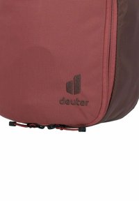 Roter Stoff-Rucksack mit strukturierten Oberflächen, ausgestattet mit einem dunkelbraunen Reißverschluss, schwarzen Akzenten und einem sichtbaren "deuter"-Logo an der Seite.