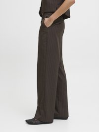 Calças castanhas risca de giz com corte direito, cintura alta e bolsos laterais. Usadas com sapatos pretos planos texturizados.