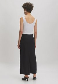 Haut sans manches blanc avec un dos en décolleté, associé à un pantalon noir à jambes larges. Le pantalon dispose de poches et d'une finition texturée. Talons noirs.