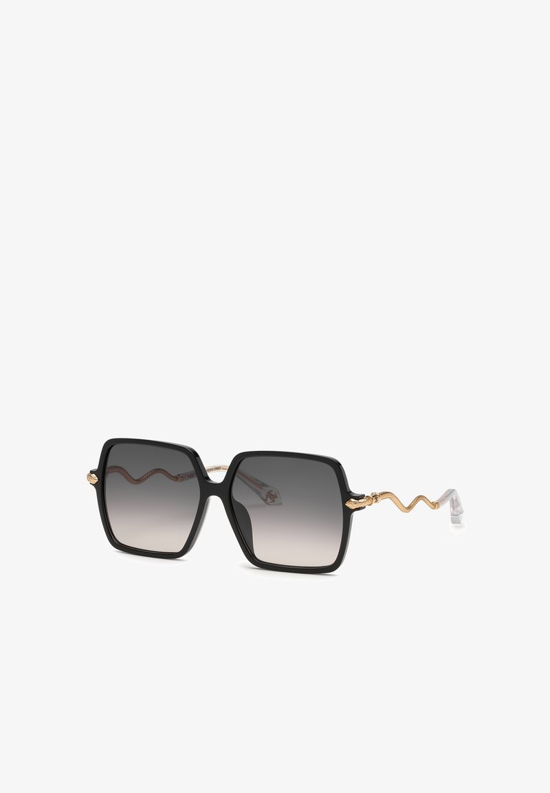 Lunettes de soleil carrées oversize noires avec verres gris dégradés et branches dorées en forme de serpent sur fond blanc.