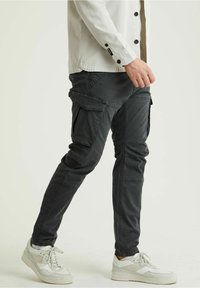 Dunkelgraue Cargo-Hosen mit mehreren Seitentaschen, schmal zulaufenden Beinen und einem strukturierten Stoff, kombiniert mit weißen Sneakers.