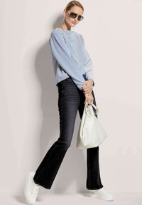 Gestreifter blauer und weißer Pullover, dunkle Schlagjeans, weiße Sneaker und eine cremefarbene Handtasche. Helles Licht betont die Texturen und Farben.