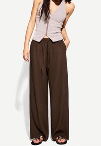 Brązowe, luźne spodnie z elastycznym pasem, połączone z dopasowaną, zapinaną na zamek, prążkowaną bluzką w jasnoróżowym kolorze. Widoczne fakturowane materiały.