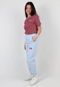 T-shirt bordeaux avec logo, jogging bleu clair avec une ceinture élastique et détails en patch, associé à des baskets blanches.
