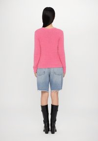 Różowy puszysty sweter, spodenki dżinsowe do połowy ud i czarne kozakki na wysokim obcasie do kolan. Sweter ma okrągły dekolt i teksturowane wykończenie.