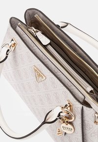 Sac à main gris et crème avec un motif monogramme, quincaillerie dorée, doubles compartiments zippés et un porte-clés décoratif. Poignées plates incluses.