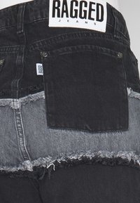 Denimjeans med en svart och grå färgblockdesign, med fransade kanter och en bakre ficka med lapplogo. Taggen säger "RAGGED JEANS."