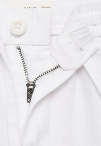 Záber na biele bavlnené nohavice zblízka, zameraný na zips a patku. Obsahuje strieborný kovový zips a biely plastový gombík.