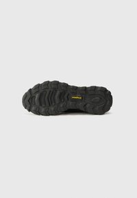 Suela de zapato deportivo negra con un patrón de tracción resistente. Presenta tacos profundos para mayor agarre y un logo de Goodyear en el costado.