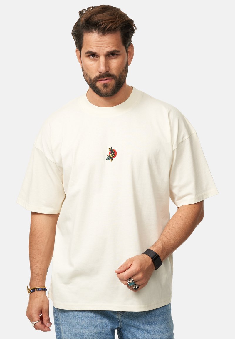 Cremfarbendes, übergroßes T-Shirt aus Baumwolle mit einem kleinen, bunten gestickten Design auf der Brust. Kurze Ärmel und runder Halsausschnitt.