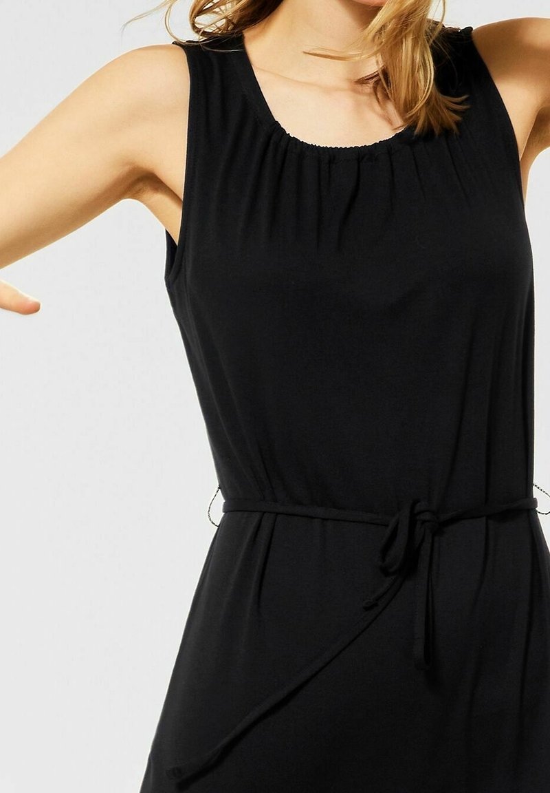 Robe noire sans manches avec un col froncé et une ceinture nouée à la taille. Tissu doux et lisse avec une forme fluide. Sans motifs ni accents.