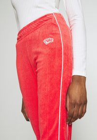 Röda sammetsbyxor med vita sidostråk och en Nike-logotyp på höften, med ett elastiskt midjeband för komfort.