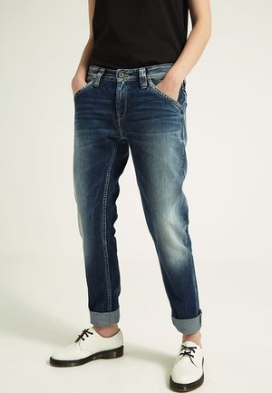 Jeans i denim i mörkblått med urtvättade områden och uppvikt fåll; har fem fickor och knappgylf. Matchas med vita skor.