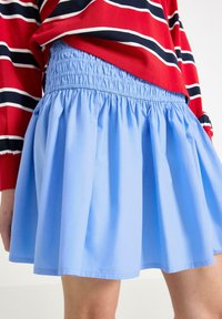 Gonna azzurra chiara con vita arricciata, caratterizzata da un design svasato e una texture liscia, stratificata per maggiore volume. Indossata con un top a righe rosse e bianche.