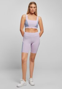 Hele lilla sportlik komplekt, mis koosneb ruudukujulise kaelusega spordirinnahoidjast ja ühtlastest kõrge vöökohaga lühikestest pükstest, millel on sinised aktsendid ja sile tekstuur.