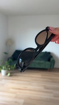 Schwarze Sonnenbrille mit dunkelbraunen Gläsern, runder Rahmenform, glattem Kunststoffmaterial und eingraviertem Logo an der Seite.