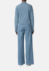 Lichtblauwe denimjack en ruime jeans. De stof is soepel, met zichtbare stiksels en twee achterzakken op de jeans.