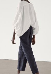 Top in lino bianco con maniche oversize, abbinato a pantaloni blu scuro. Il tessuto ha una consistenza morbida e il design presenta una vestibilità rilassata.