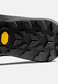 Svart Vibram yttersula med en robust, texturerad yta och framträdande sulor för grepp. Hexagonala mönster och en gul Vibram-logotyp framhäver designen.