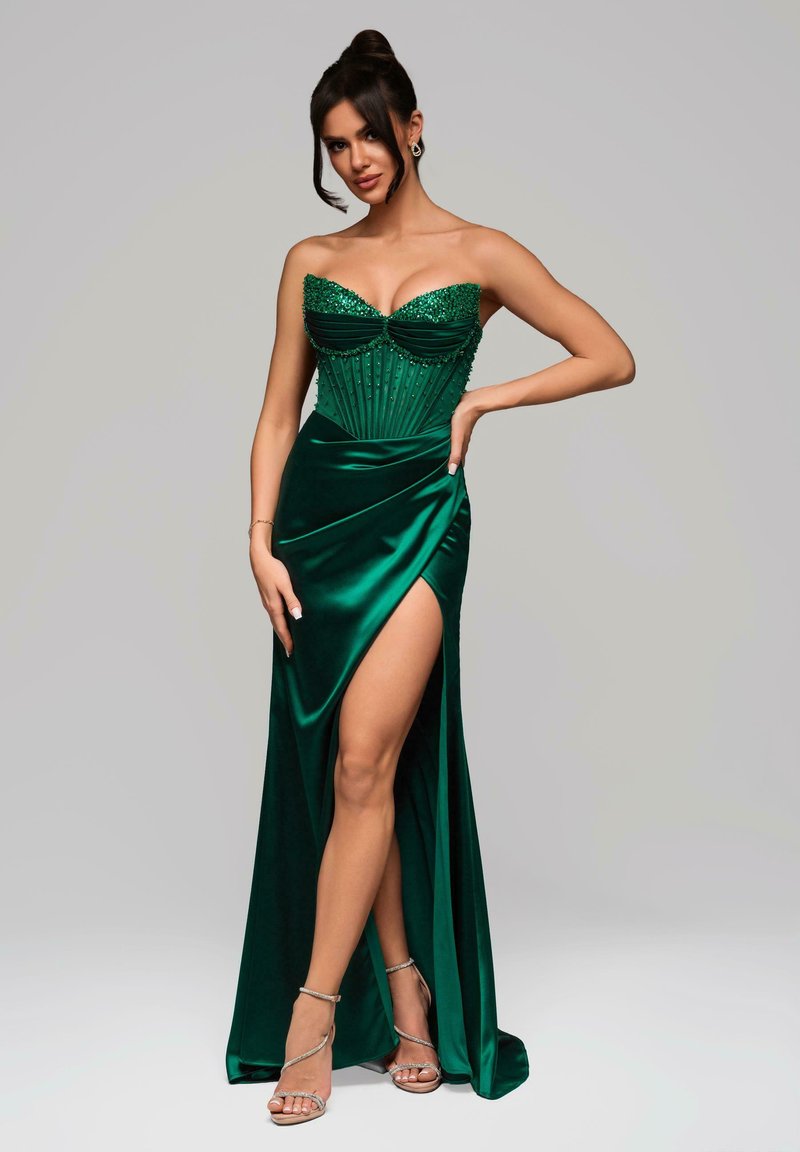 Grünes Satin-Kleid mit einem trägerlosen Oberteil, das mit Pailletten verziert ist, einer gefalteten Taille und einem hohen Schlitz. Kombiniert mit silbernen Riemchensandalen.
