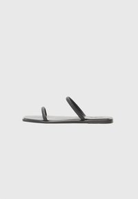 Svarte flate sandaler med to slanke stropper, laget av glatt materiale. Har en rektangulær såle og en teksturert stropp. Minimalistisk design.