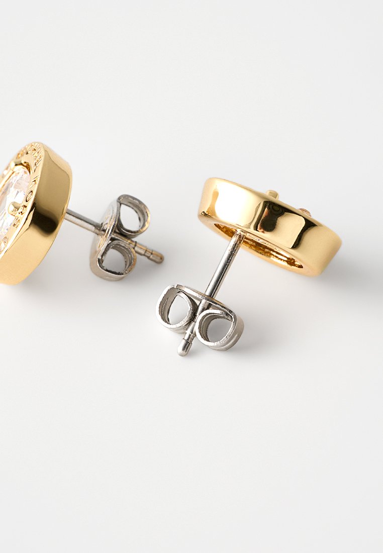 Pendientes de stud de oro y plata con un diseño circular, textura suave y un acento de piedra central clara en un engaste de garras.