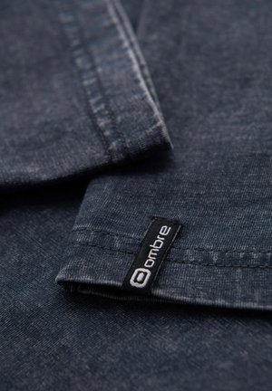 Dunkelblauer Denim-Stoff mit einer glatten Textur, ausgestattet mit einem schwarzen Etikett mit weißem Text, der "ombre" nahe der Naht liest.