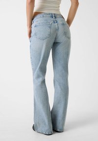 Jasnoniebieskie spodnie dzwony z wyblakłą fakturą, wyposażone w dwie tylne kieszenie i średni stan. Detale ze szwem na dole dodają wyrazu.