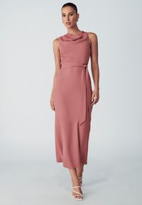 Dusty rose, sleeveless dress with cowl neckline, tie belt at the waist, and flowing midi length. Smooth, lightweight fabric. Strappy white sandals.