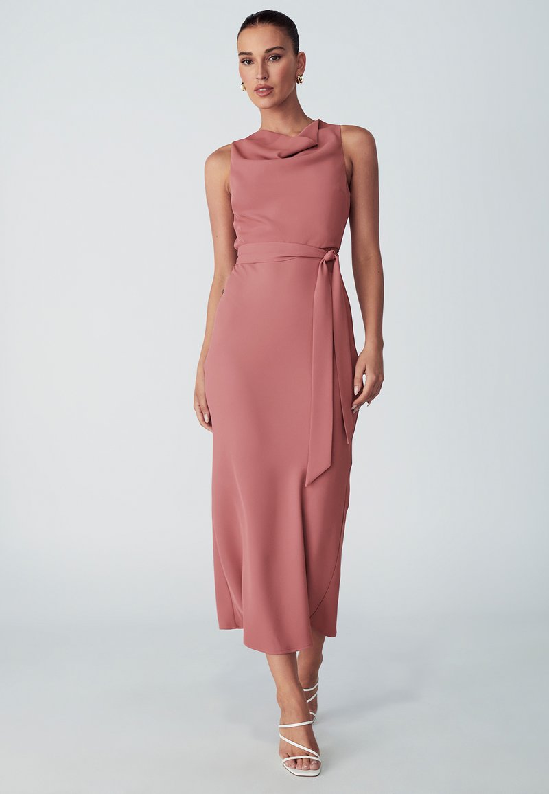 Dusty rose, sleeveless dress with cowl neckline, tie belt at the waist, and flowing midi length. Smooth, lightweight fabric. Strappy white sandals.