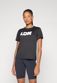 T-shirt noir à manches courtes avec "LDN" en lettres blanches. Il présente un col rond et une coupe décontractée, associé à un short de cyclisme foncé.