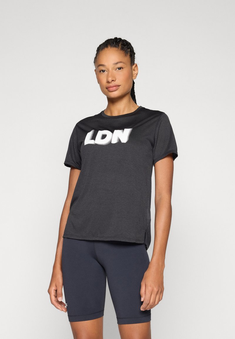 T-shirt noir à manches courtes avec "LDN" en lettres blanches. Il présente un col rond et une coupe décontractée, associé à un short de cyclisme foncé.