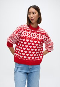 Suéter de punto rojo con un patrón de corazones blancos y texto XOXO. Mangas largas con puños y dobladillo acanalados, textura suave. Corte clásico.