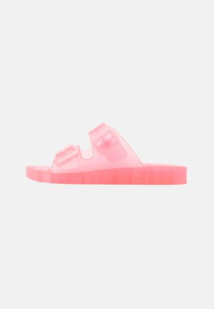 Ροζ διάφανη σαγιονάρα με δύο ρυθμιζόμενους ιμάντες με αγκράφες και επίπεδη σόλα σε απλό φωτεινό φόντο.