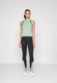 Light green athletic tank top with black accents and "ENDLESS" text. Black leggings with light green panels at the ankles. White sneakers.