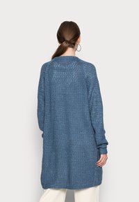 Larga chaqueta de punto en un tono azul con un patrón texturizado. Presenta un escote de barco y puños acanalados, diseñada para un ajuste holgado.