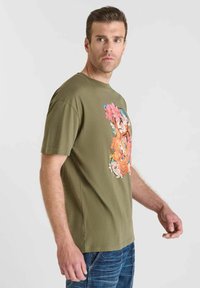Camiseta de algodón verde oliva con un estampado floral en la parte frontal en rosa, naranja y azul. Manga corta y diseño de cuello redondo.