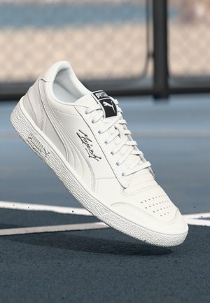 Sneaker in pelle bianca con punta perforata, suola in gomma testurizzata, logo nero sulla linguetta e accenti laterali. Design classico con chiusura a lacci.