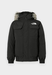 Veste d'hiver noire isolante avec capuche doublée de fourrure grise, deux poches à rabat sur la poitrine, poignets côtelés et logo The North Face sur la poitrine.