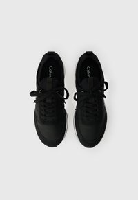 Adidași negri cu un amestec de țesătură netedă și texturată, șireturi rotunde și detalii albe pe talpă. Prezintă un logo pe branț.