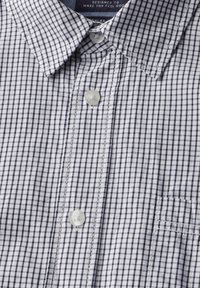 Knappskjorta med ett mönster i vitt och marinblått rutigt, en spetsig krage och en bröstficka. Slät tygtextur.