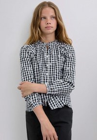 Camisa de cuadros en blanco y negro con cuello con volantes, mangas largas y acentos de bordado floral en la tela.