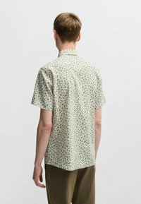 Camicia a maniche corte di colore verde chiaro con un piccolo motivo floreale ripetuto. Colletto button-down, vestibilità rilassata e materiale leggero in cotone.
