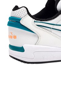 Sneaker bianca in pelle con dettagli turchesi, rivestimento in suede nero, tomaia perforata e un logo arancione audace sul tallone. Suola in gomma.