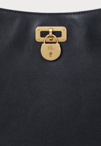 Mustapahuisin laukku, jossa on kultainen padlock ja metalliosat. Pinnassa on sileä kehys, hienovarainen rakenne ja minimaalinen ompelutaito.