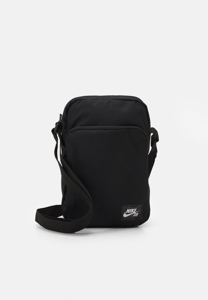 Borsa a tracolla nera in nylon con cinturino regolabile, chiusura a zip e una piccola toppa del logo Nike SB sul davanti. Forma rettangolare.