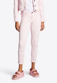 Jeans de mezclilla rosa claro con un diseño ajustado, tobillos con dobladillo y bolsillos frontales, combinados con sandalias rosa claro con un detalle de lazo.