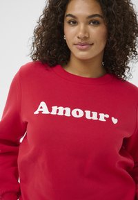 Rotes Sweatshirt aus Baumwollmischung, mit dem Schriftzug "Amour" in weißen, fetten Buchstaben und einem kleinen Herz darunter. Rundhalsausschnitt, lange Ärmel.
