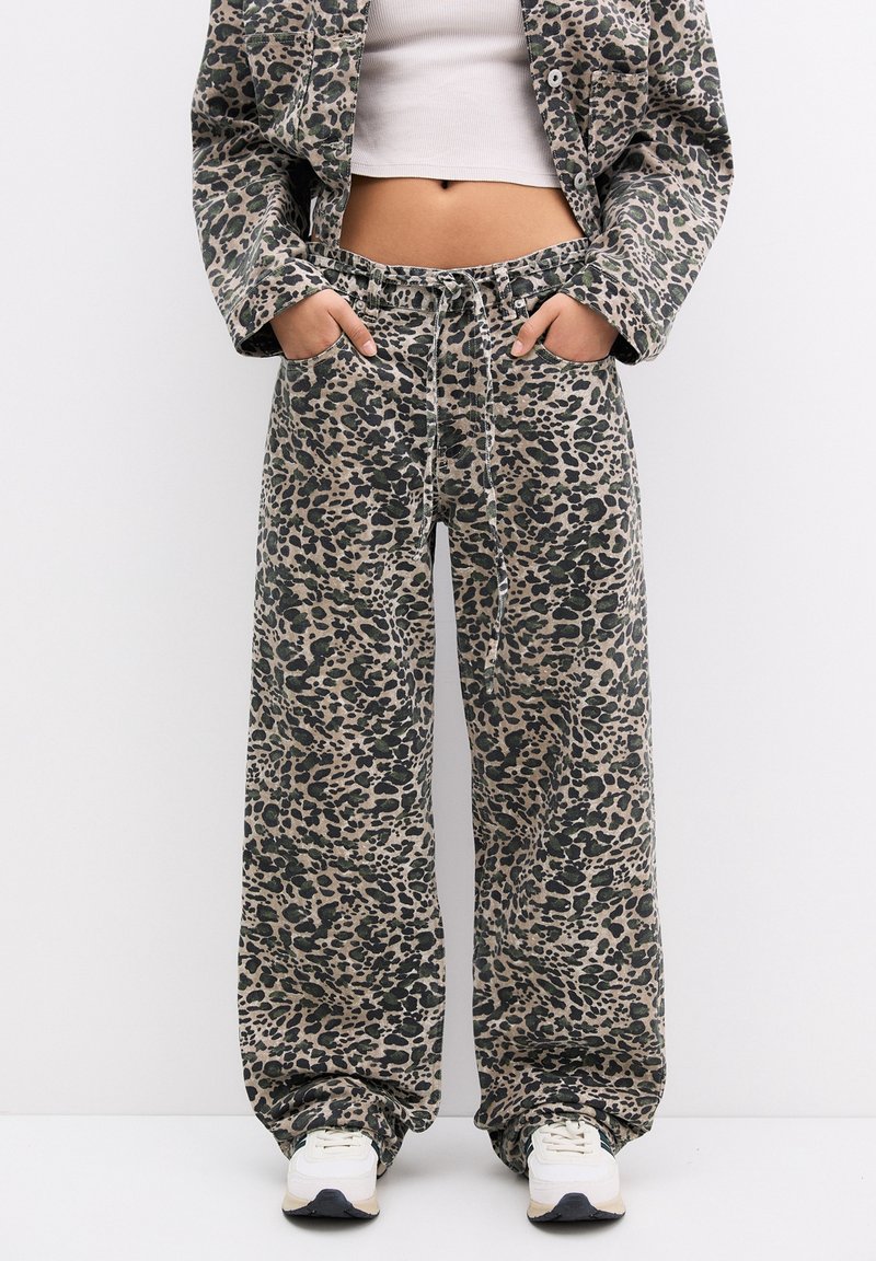 Pantalon large à imprimé léopard avec taille à cordon porté avec une veste assortie, un top court blanc et des baskets blanches.