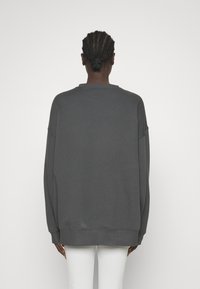 Grå oversized sweatshirt med rund halsringning, sänkt axelsöm och ribbade ärmslut. Slät textur med avslappnad passform; minimalistisk design.
